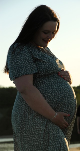 Linda guckt an sich herab und hält ihren kugelrunden Babybauch